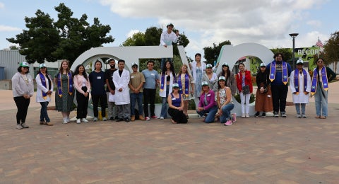 A group of students in graduation regalia posing in front of large letters, "EVC".