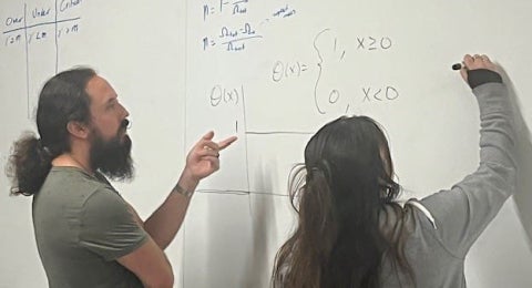 Two people working through an equation on a whiteboard.